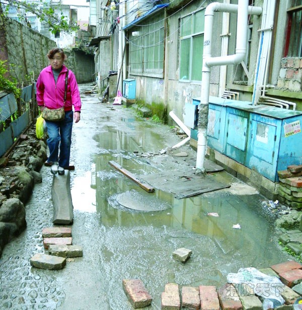 平安巷14棟26號樓，一位女士正小心翼翼地從木板上通過。